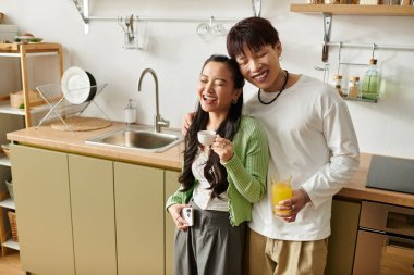 Gülümseyen çift şık bir mutfakta duruyor, kahvaltı içkileriyle keyifli anları paylaşıyorlar..