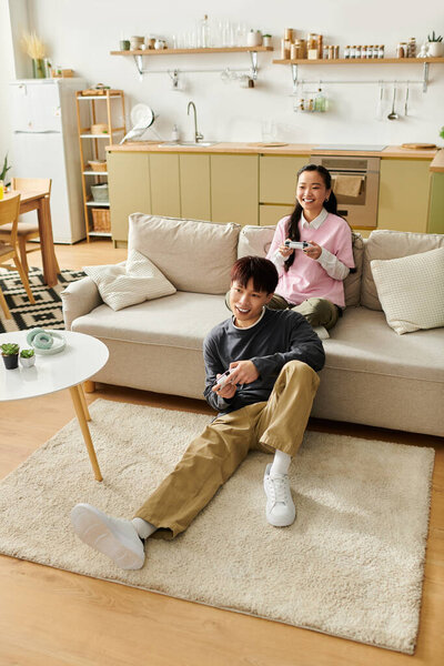 A young Asian couple relaxes on the sofa, playing games and sharing smiles at home.