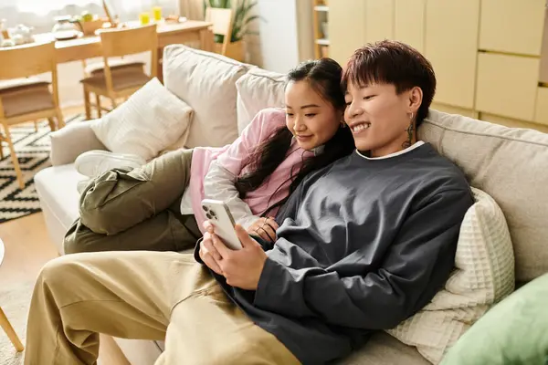 Çift, rahat bir yaşam alanında akıllı telefonlarıyla büyülenmiş bir şekilde koltukta keyifli bir anı paylaşıyor..