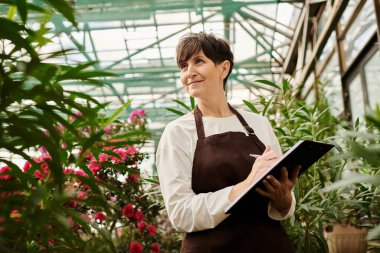 Yeşilliklerin arasında özenle çalışan kendine güvenen bir kadın bitkilerini dikkatle izliyor..