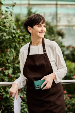 Kendine güveni tam bir kadın, yemyeşil bitkiler ve çiçeklerle çevrili canlı bir serada çalışmaktan hoşlanıyor.