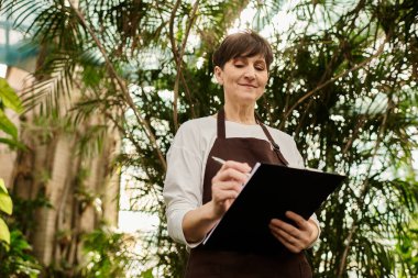 Olgun bir kadın, bitkilerle çevrili canlı bir serada görevlerini zevkle yerine getirir..