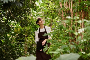 Serada filizlenen bitkiler arasında çalışırken kısa saçlı olgun bir kadın gülümsüyor..