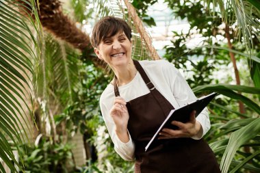 Kendine güvenen olgun bir kadın, yemyeşil bir seranın içinde işiyle meşgul..