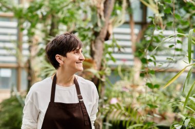 Kendine güvenen olgun bir kadın, sera atmosferindeki yemyeşil bitkilerin arasında işinden zevk alıyor.