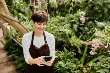Seradaki kendine güveni tam bir kadın akıllı telefonunu yemyeşil ve çiçeklerin arasında kullanır..