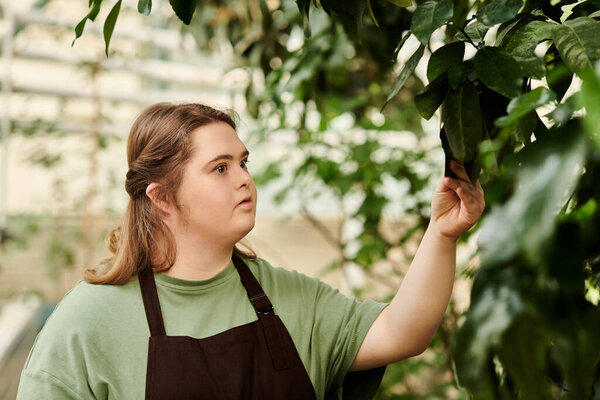 Young woman with Down syndrome is actively tending to lush plants in a greenhouse setting.