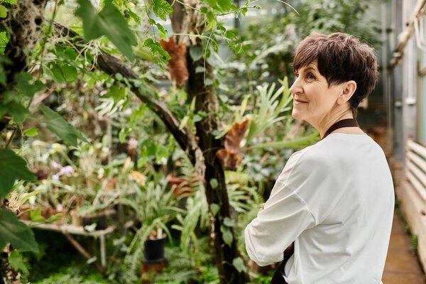 A confident woman nurtures plants in a vibrant, thriving greenhouse.