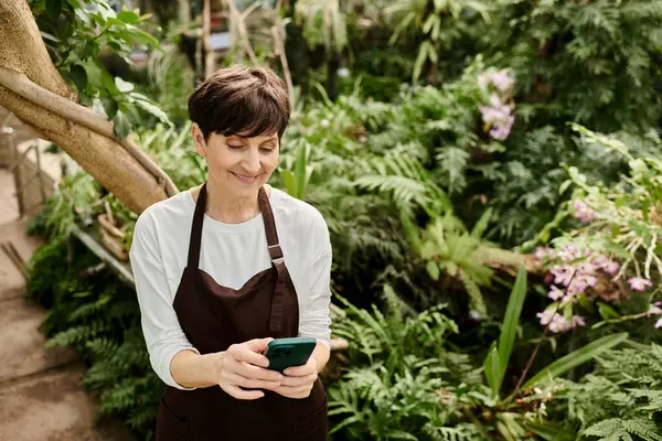 Seradaki kendine güveni tam bir kadın akıllı telefonunu yemyeşil ve çiçeklerin arasında kullanır..