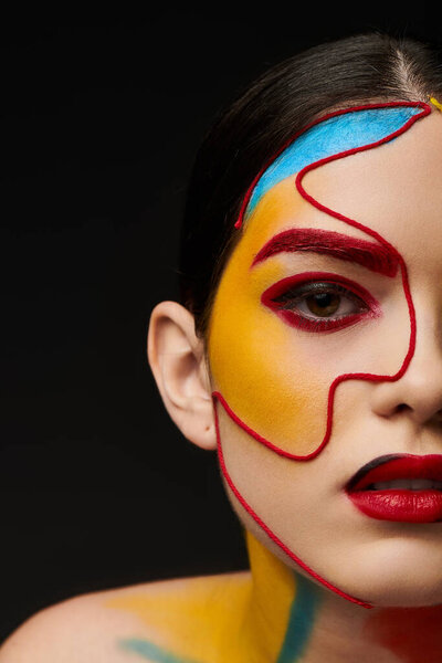 Молодая красивая женщина демонстрирует яркое искусство лица, которое улучшает ее черты с игривыми цветами.