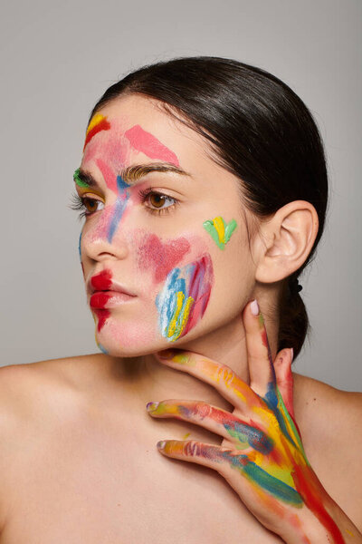 Молодая женщина демонстрирует свое творчество с красочным лицом и раскрашенными руками.