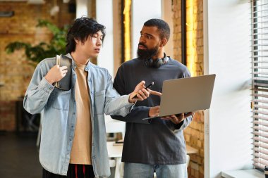 İki profesyonel, modern bir ofiste dizüstü bilgisayarla iş tartışır..