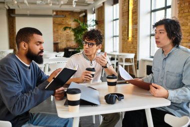 Üç profesyonel, şık bir çalışma alanında fikir ve kahve paylaşımı yaparak iş birliği yapıyor..
