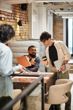 Meslektaşlar açık ofis içinde üretken bir tartışmada fikir ve teknolojiyi paylaşırlar..