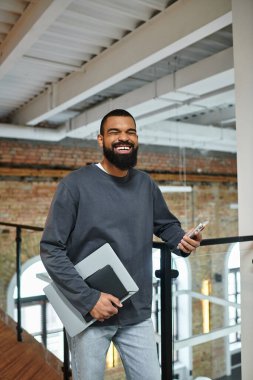 Bilgisayarlı ve telefonlu gülümseyen şahıs çağdaş çalışma alanının keyfini çıkarıyor..