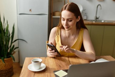 Genç bir kadın modern bir mutfakta akıllı telefonuna bakarken kahvesinden zevk alır..