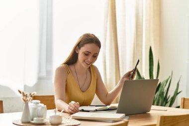 Genç ve güzel bir kadın dizüstü bilgisayarını parlak bir alanda kullanırken notlar yazarken gülümsüyor..