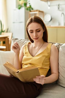 Evdeki rahat bir kanepede dinlenirken kendini bir kitaba kaptırmış güzel bir genç kadın..