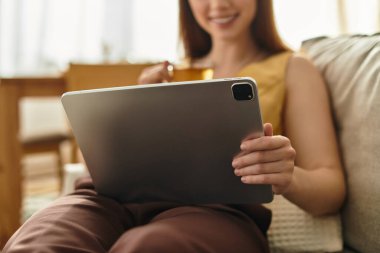 Genç ve güzel bir kadın, tablet üzerinde gezinirken çayından zevk alıyor, rahatlıyor..