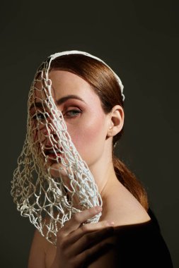 Çekici genç bir kadın zarif bir şekilde yumuşak gölgelerle aydınlatılmış yaratıcı bir başlık sergiliyor..