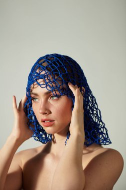 Genç ve güzel bir kadın çarpıcı mavi bir başlık sergiliyor, büyüleyici özelliklerini vurguluyor..