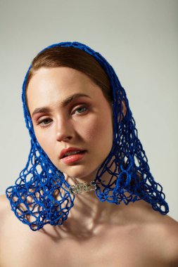 Genç bir kadın zarifçe poz verir, canlı mavi bir atkıyla süslenir ve güzelliğini ön plana çıkarır..