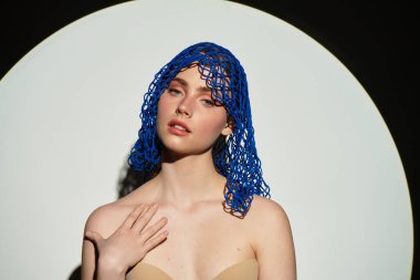 Çekici genç bir kadın zarif pozlar veriyor. Yumuşak ışıklandırmayla çerçevelenmiş yaratıcı mavi bir başlıkla..