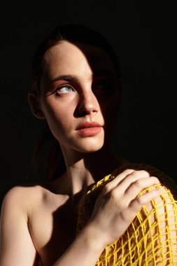 Genç bir kadın, çarpıcı bir kontrast için parlak sarı kumaşa sarılmış, düşünceli bir şekilde bakar..