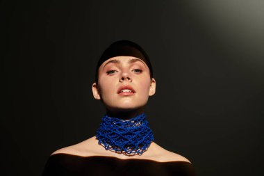 Kendine güvenen genç bir kadın zarif poz verir, spot ışıklarında çarpıcı mavi bir yaka takar..