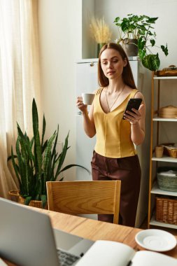 Bitkilerle dolu sıcacık bir yerde, genç bir kadın akıllı telefonunu kontrol ederken kahvenin tadını çıkarıyor..