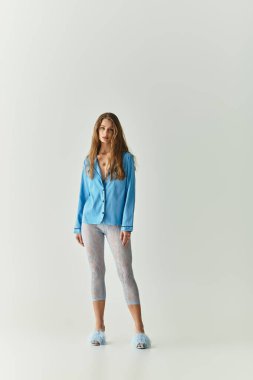 Genç bir kadın, mavi bir hırka ve şık taytlar giyerek, aydınlık bir odada güven içinde poz veriyor..