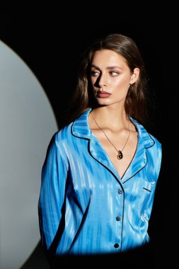 Uzun saçlı genç bir kadın, sanatsal aydınlatmaya karşı mavi kıyafetiyle güzelliğini sergiliyor..