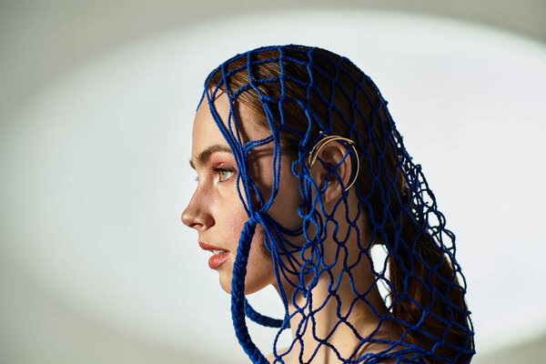 A young woman poses gracefully in a striking blue net headpiece, showcasing fashion artistry.