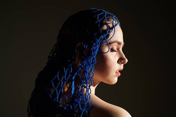 A young woman with serene expression showcases intricate blue art, illuminated in soft shadows.