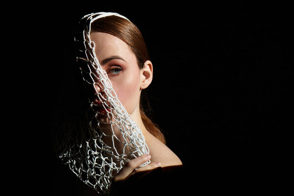 Молодая женщина изящно держит кружева, которые частично покрывают ее лицо, настроены против тьмы.