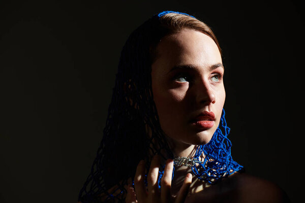 Молодая женщина в синем кружеве шарф очаровывает в темном, художественном окружении.