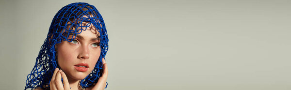 Поразительный синий головной убор украшает молодую красивую женщину, как она вдумчиво смотрит, создавая интригу