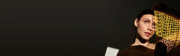 Молодая женщина игриво взаимодействует с желтой сеткой в творческом, тускло освещенном пространстве..