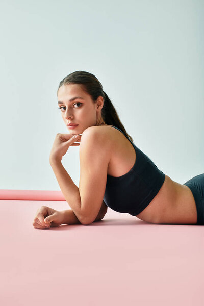 A young woman lies on a soft pink surface, exuding confidence in a serene setting.
