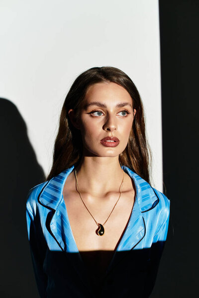 A young beautiful woman stands confidently in a vibrant blue outfit, illuminated by soft shadows.