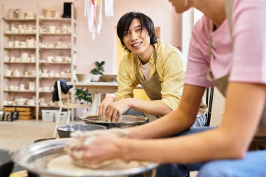 Çömlek atölyesinde, genç bir çift kil şekillendirirken gülümser ve birlikte güzel sanatlar yaratırlar..
