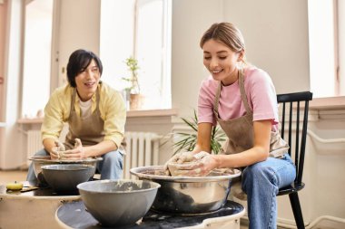 Genç çiftler kil kalıpları çıkarır ve parlak, yaratıcı bir çömlek atölyesinde gülümserler..