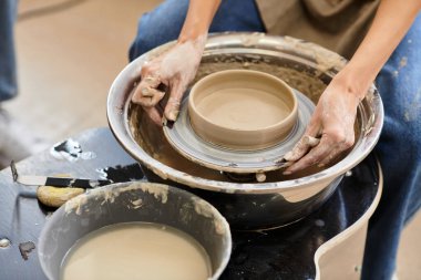 Yaratıcı araç gereçler ve malzemelerle çevrili bir çömlek çarkının üzerindeki kilden bir kaseyi ustalıkla şekillendirir..