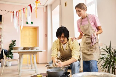 Genç bir çift çömlek atölyesinde eğleniyor. Tekerlek üzerinde kil şekillendirirken gülümsüyorlar..