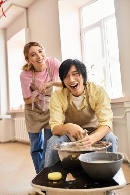 Güneşli bir çömlek atölyesinde neşeli bir şekilde kil şekillendiren genç bir çift gülümsüyor..