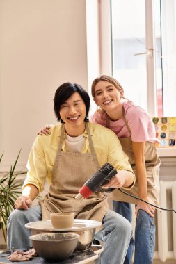 Genç bir çift, çömlek atölyesinde birlikte güler ve kil şekillendirir..