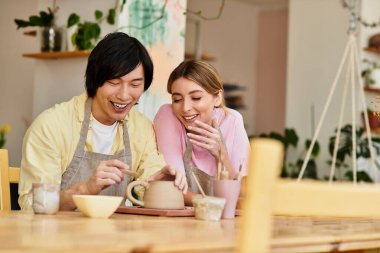Genç bir çift, neşeli bir stüdyoda çömlek yaparken kahkahalarını paylaşıyor..