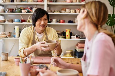 Genç bir çift çömlek atölyesinde kil şekillendiriyor, sanat yaparken kahkaha ve neşe paylaşıyorlar..