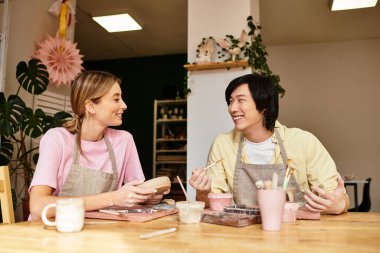 Genç bir çift, gülücükler ve sanatsal fikirler alışverişinde bulunurken eğlenceli bir çömlekçilik seansından zevk alır.