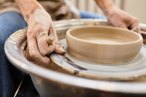 Hands expertly shape clay on the potters wheel in a bright and inviting pottery studio.